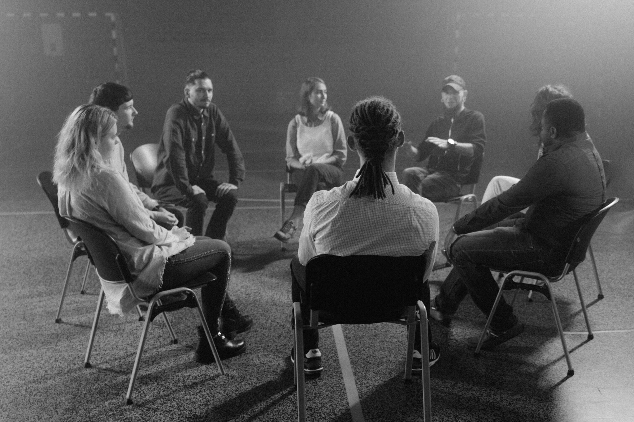 A diverse group of people in a circle discussing and supporting each other in a therapy session.